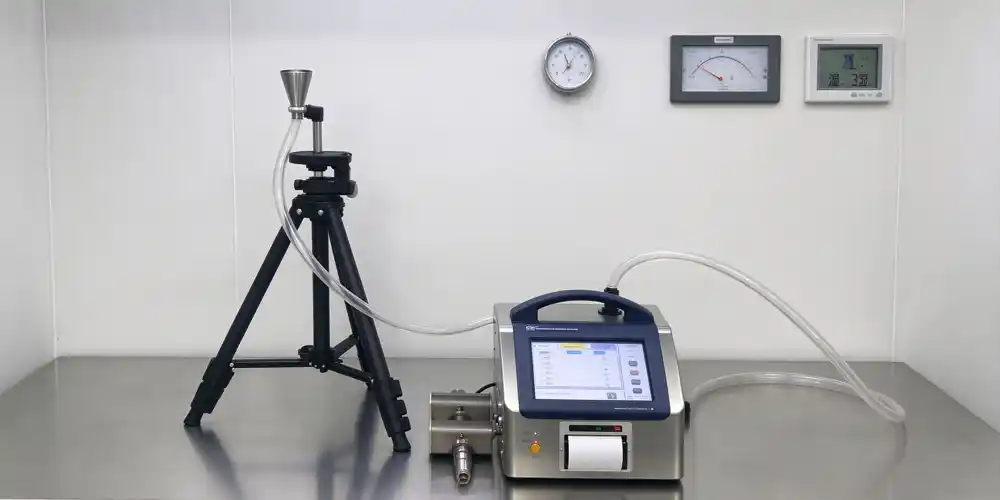 Portable airborne particle counter with tripod sampling probe and differential pressure gauges on cleanroom wall