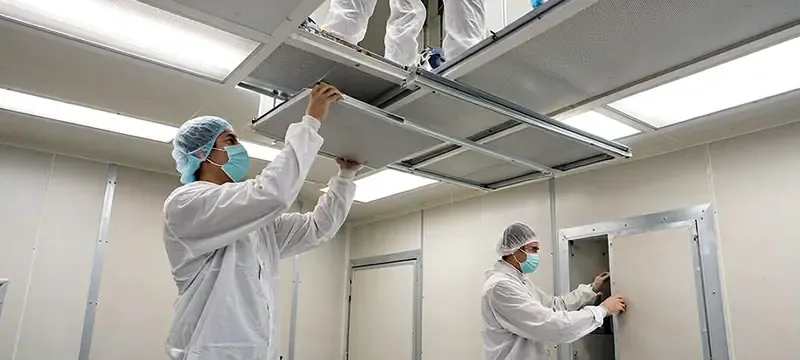 Technicians servicing ceiling filters and service hatches above a hardwall clean room