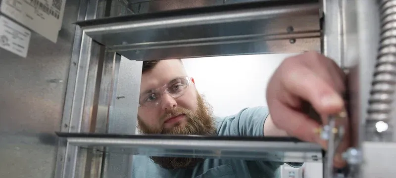 Technician inspecting a fire damper inside an air handling unit Technician inspecting a fire damper inside an air handling unit