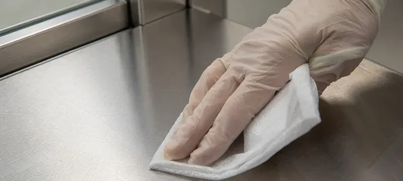 Gloved hand wiping the stainless face of a cleanroom door with a non-woven wipe